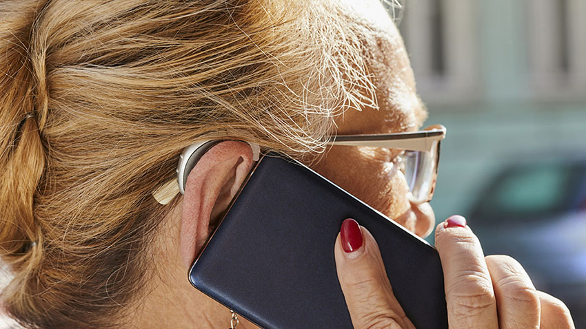 Close-up of senior woman with hearing aid using smartphone