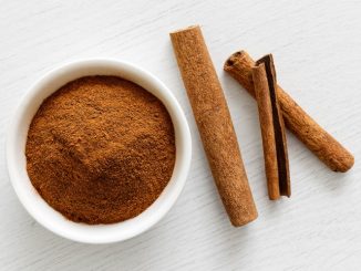 Finely ground cinnamon in white ceramic bowl isolated on white wood background from above. Cinnamon sticks.